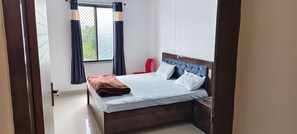 A bedroom with a bed, a nightstand, a chair, and a window with curtains.