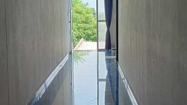 A corridor with a reflective floor, a door on the left, and a window with curtains on the right.