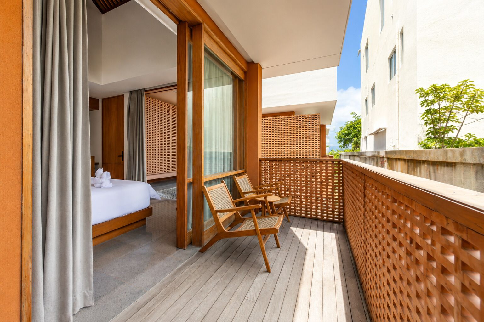 A balcony with a bed, wooden chairs, and a wooden lattice partition.