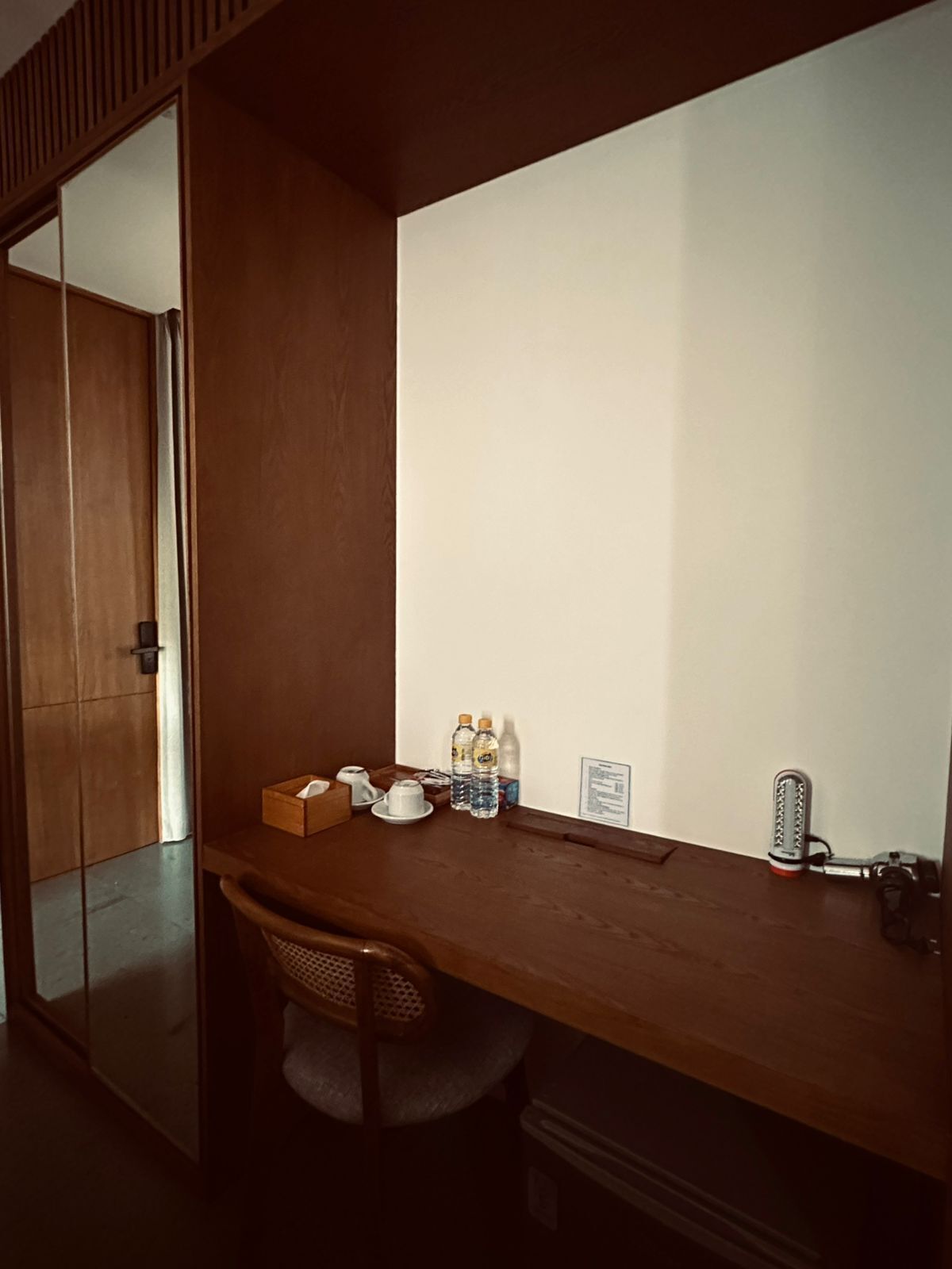 A small, private office with a wooden desk, a chair, and a large mirror. There are two bottles of water and a tissue box on the desk.