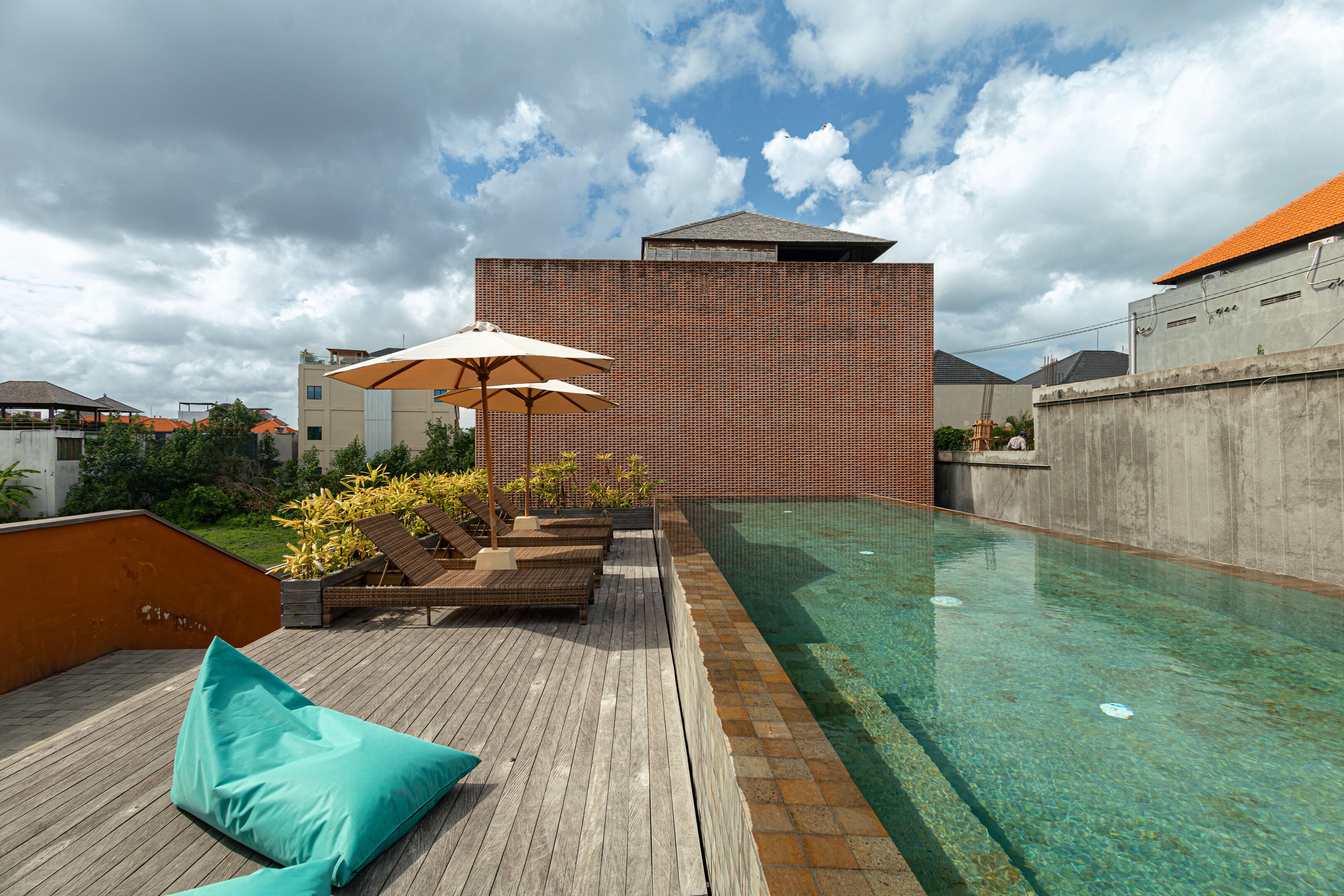 A rooftop pool area with lounge chairs and umbrellas, surrounded by a high-rise building.