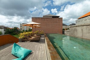 Uma área de piscina no terraço, com espreguiçadeiras e guarda-sóis, rodeada por um edifício alto.