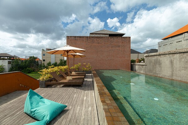 A rooftop pool area with lounge chairs and umbrellas, surrounded by a high-rise building. - Jaladhi Echo Beach Villa (Canggu)
