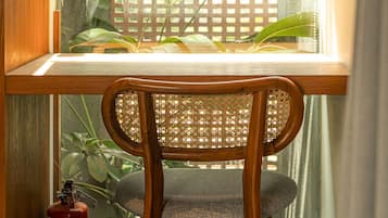 A wooden chair with a woven backrest positioned at a window with a view of a wooden fence and greenery outside.