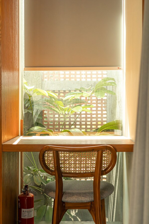A wooden chair with a woven backrest positioned at a window with a view of a wooden fence and greenery outside. - Jaladhi Echo Beach Villa (Canggu)