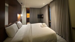 A hotel room with a large bed, a flat-screen TV mounted on the wall, and a balcony with curtains. - Jaladhi Echo Beach Villa (Canggu)