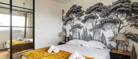 A hotel room with a bed, a nightstand, a lamp, a mirror, and a wall with a tree mural.