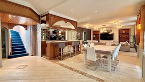 A spacious living area with a bar, a dining table, and a sofa. A staircase is visible on the left. - L'Orée des Rêves et des Mets (Vibraye)