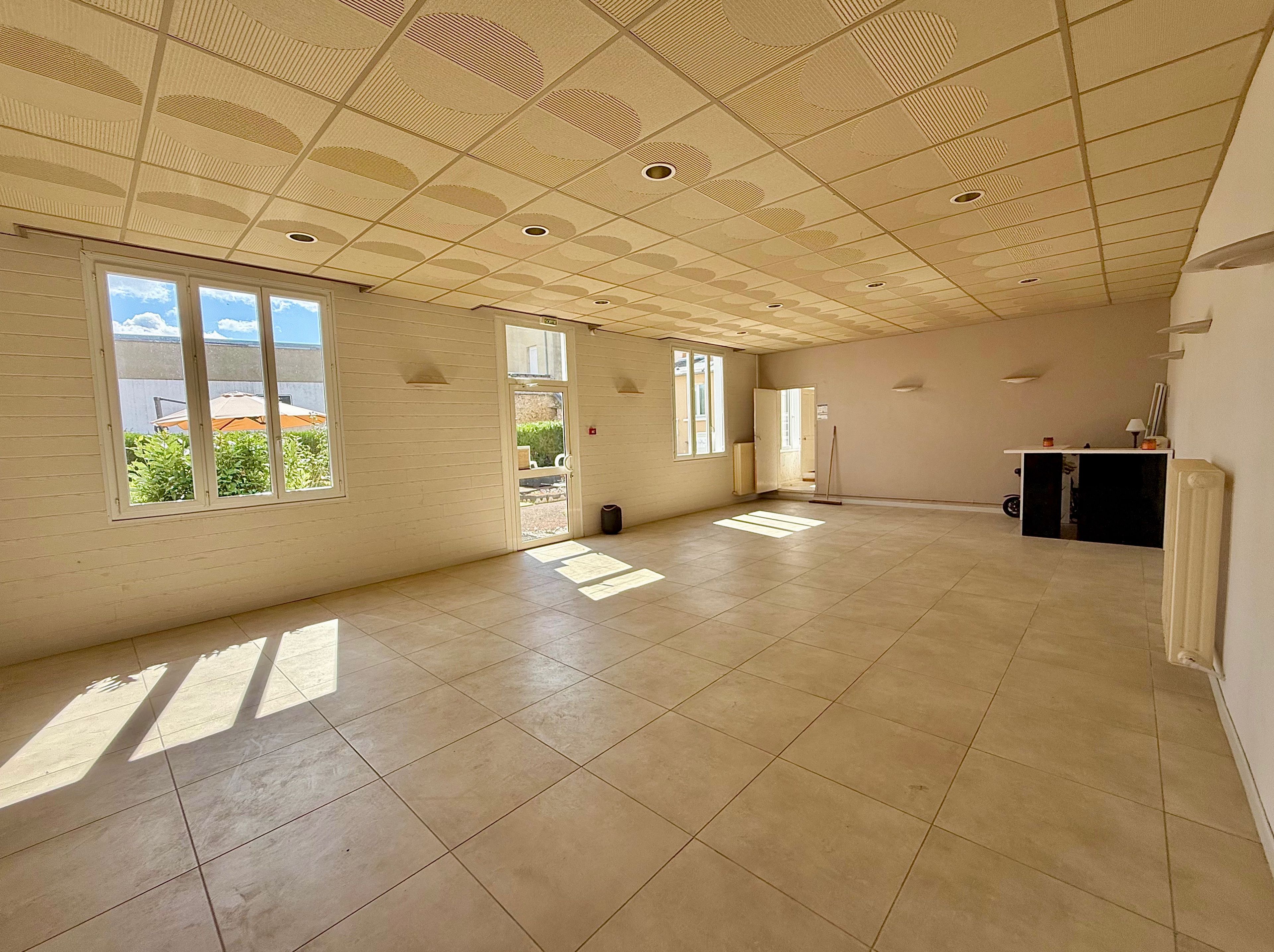 A spacious room with large windows, a tiled floor, and a ceiling with a grid pattern.
