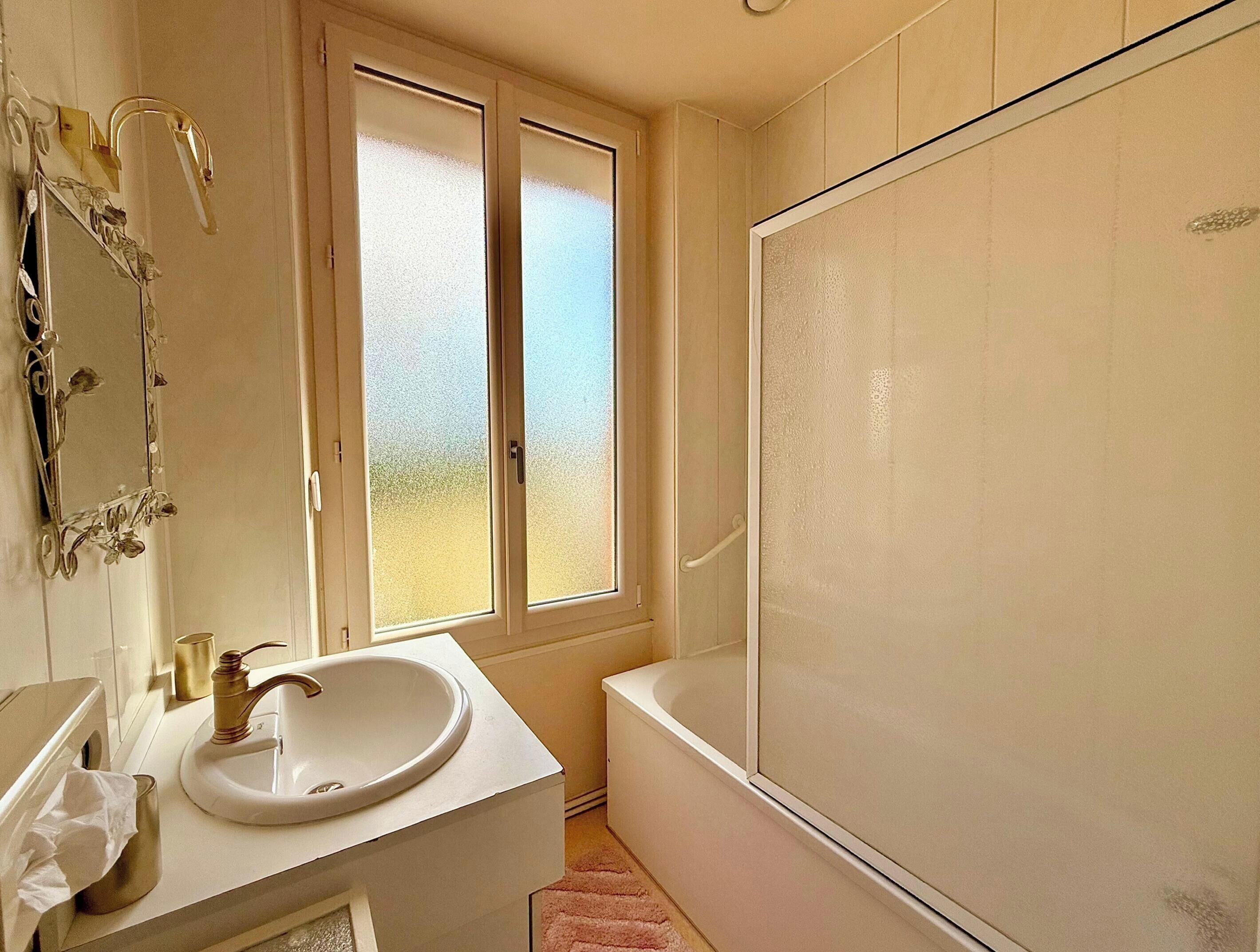 Un bagno con un lavandino bianco, uno specchio con decorazioni, porte in vetro satinato e una vasca da bagno.