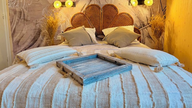A bed with a wooden headboard, multiple pillows, and a woven bedspread. - L'Orée des Rêves et des Mets (Vibraye)