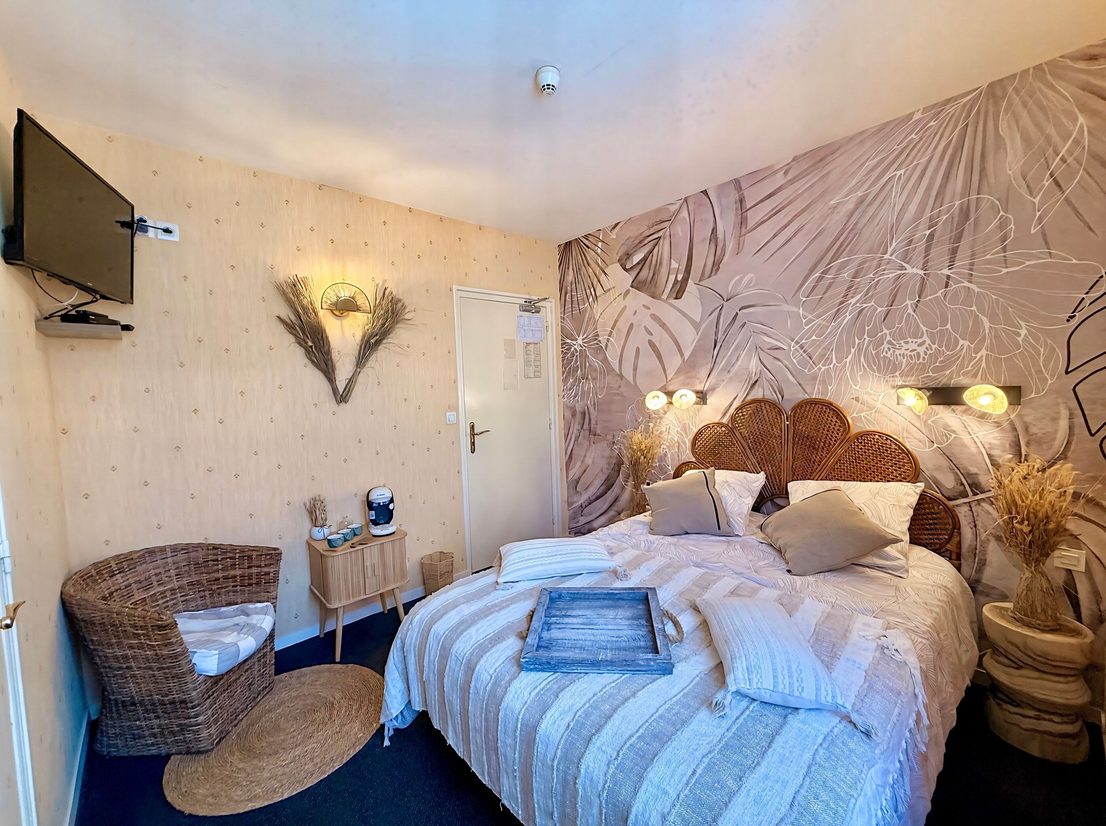 A bedroom with a bed, a television, a wall-mounted light, a door, and a decorative wall piece.
