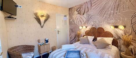 A bedroom with a bed, a television, a wall-mounted light, a door, and a decorative wall piece.