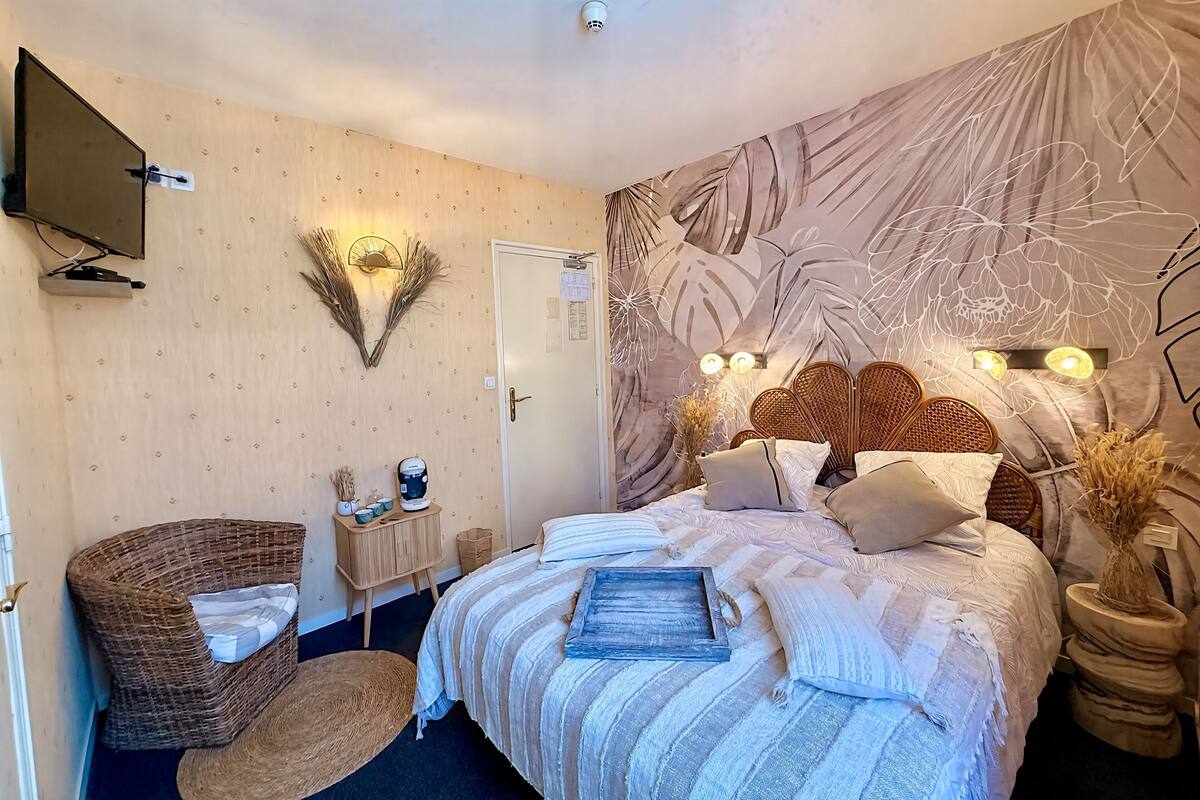 A bedroom with a bed, a television, a wall-mounted light, a door, and a decorative wall piece.