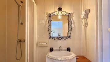 A bathroom with a shower, a sink with a marble countertop, a mirror with a decorative frame, and a hairdryer mounted on the wall.