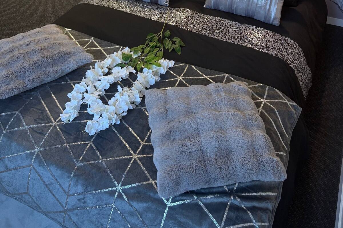 A bedroom with a bed featuring a geometric patterned bedspread, multiple pillows, and a decorative branch with white flowers.