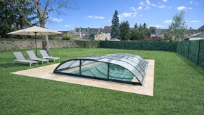 A greenhouse structure on a lawn with lounge chairs and a stone wall in the background. - L'Orée des Rêves et des Mets (Vibraye)