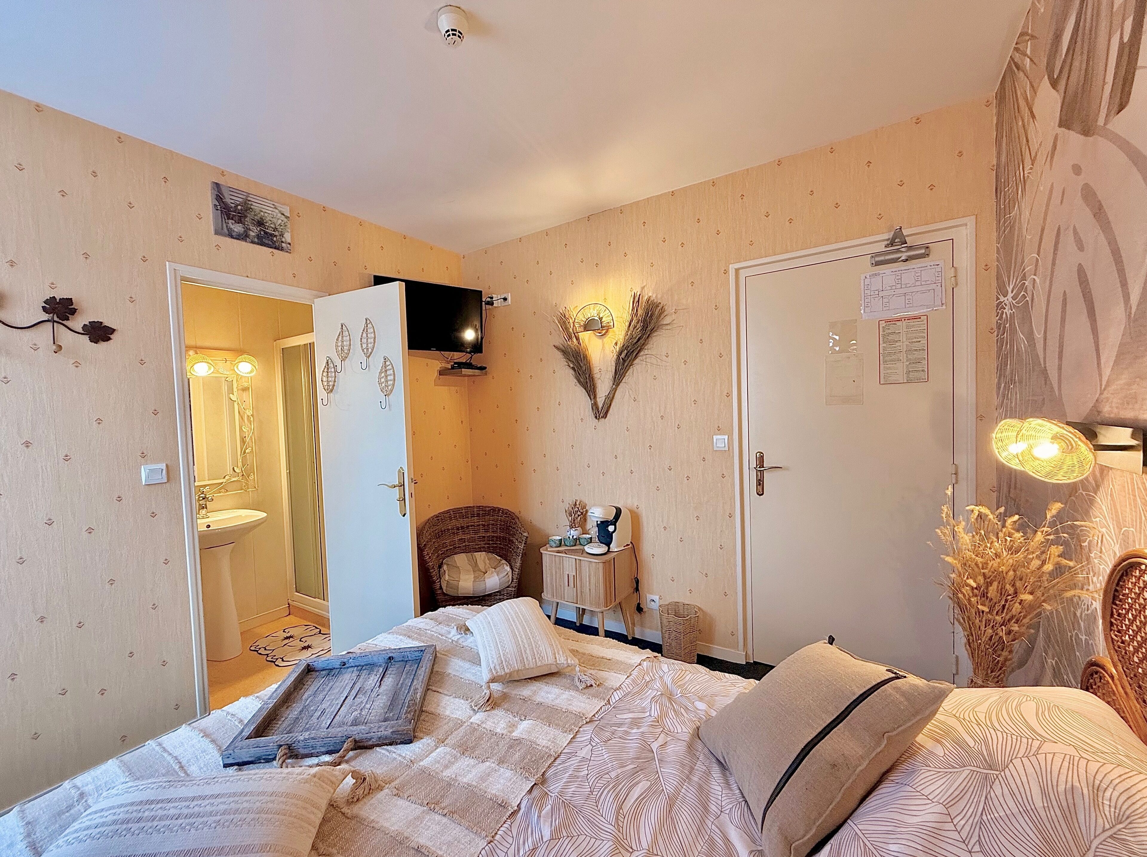Un dormitorio con cama, mesita de noche, espejo, televisor de pared y puerta que da a un baño.