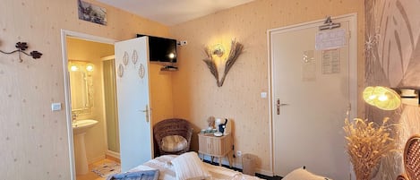 Un dormitorio con cama, mesita de noche, espejo, televisor de pared y puerta que da a un baño.