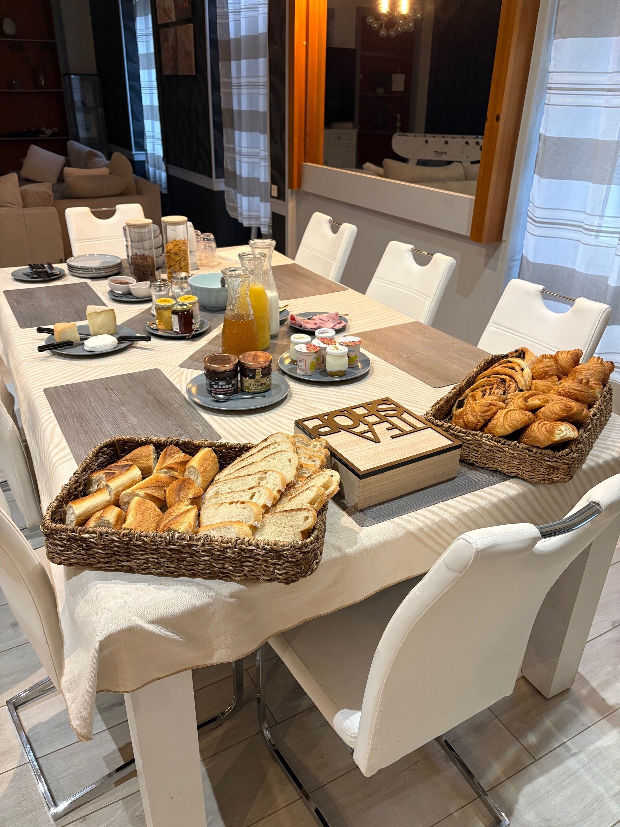 Un bufé de desayuno con pan, bollería y diferentes salsas sobre una mesa en un comedor moderno.