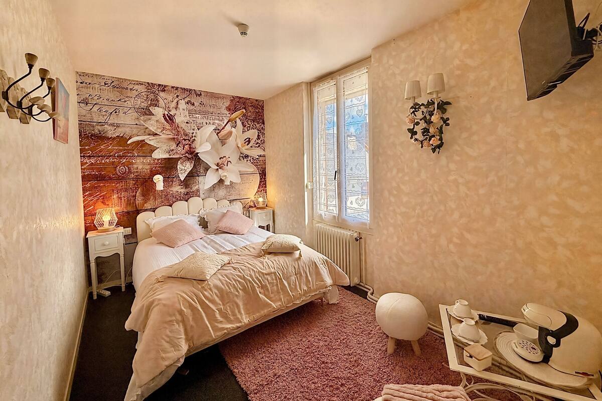 A bedroom with a large bed, a nightstand, a dresser, a radiator, a window with decorative glass, and a wall-mounted TV.