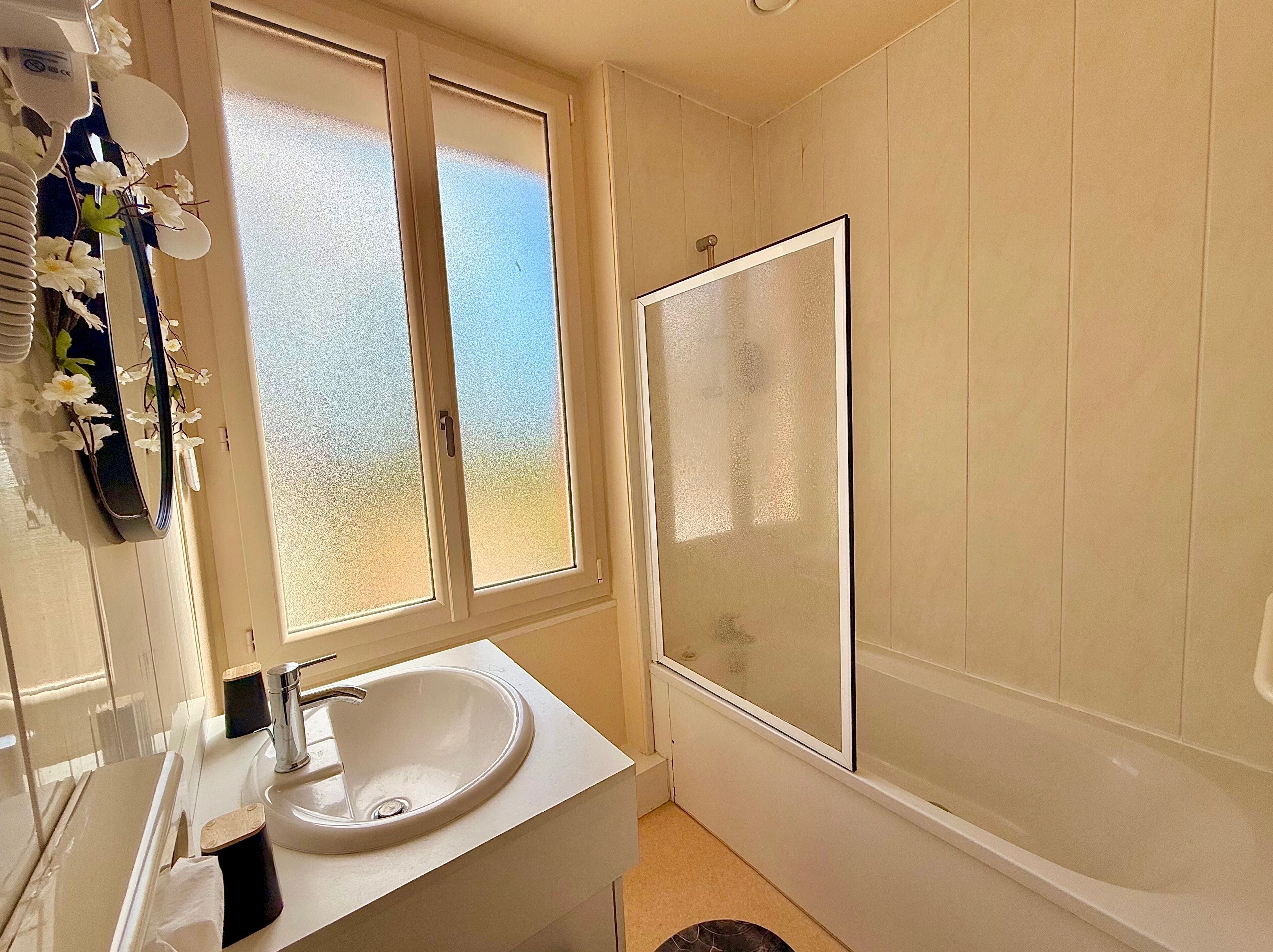A bathroom with a white sink, a mirror, a window, and a bathtub.
