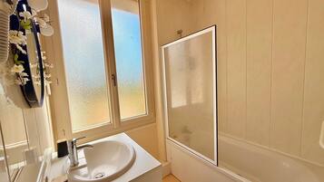 A bathroom with a white sink, a mirror, a window, and a bathtub.
