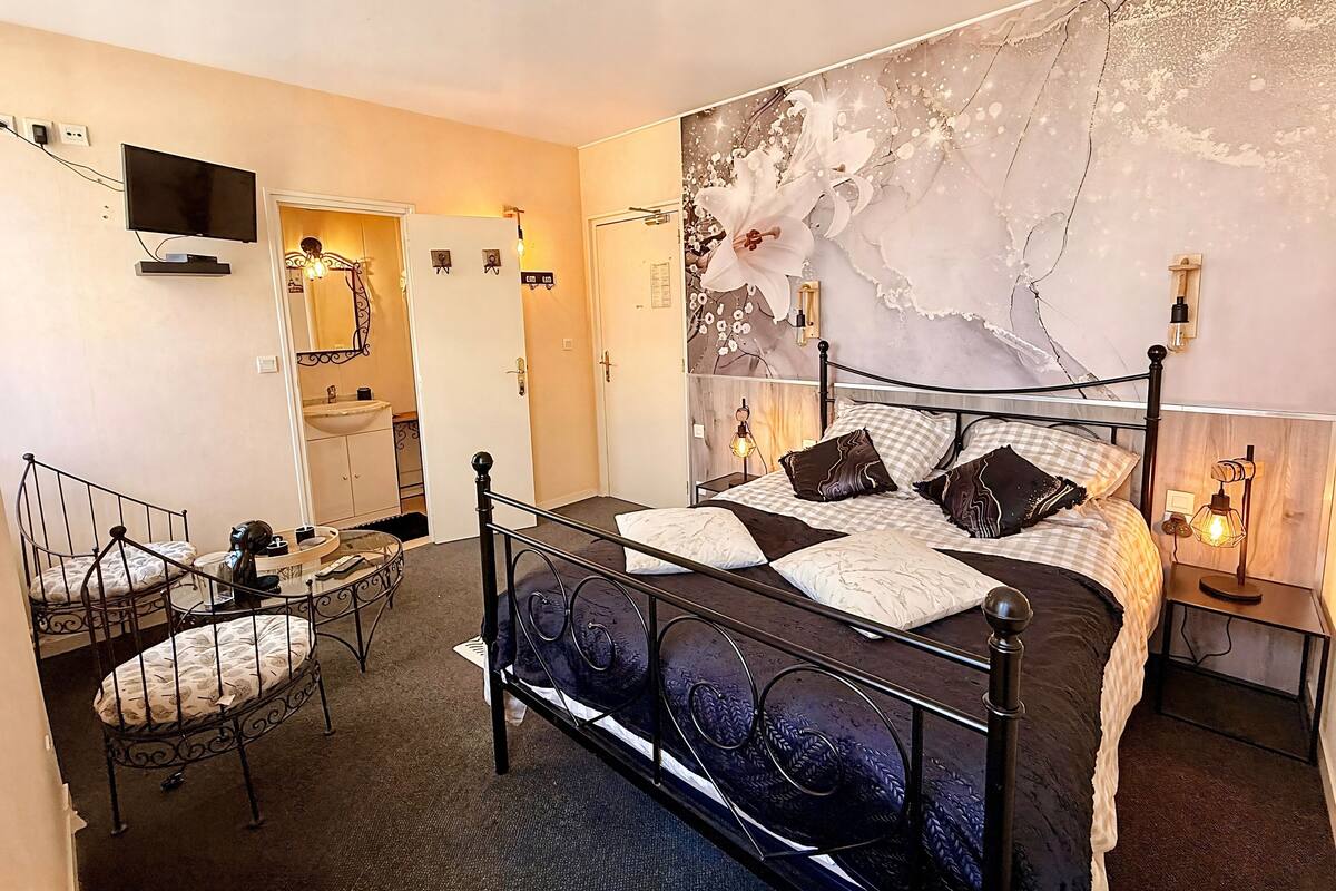 A bedroom with a bed, a desk, a chair, a mirror, and a wall-mounted TV.