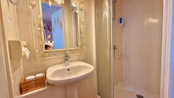 A bathroom with a white sink, a mirror with leaf decorations, and a glass-enclosed shower.