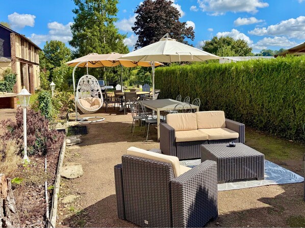 Un espace extérieur aménagé en terrasse, avec des meubles en osier, une table à manger et un fauteuil suspendu.