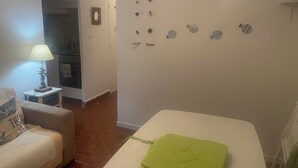 Une chambre avec un lit blanc, une petite table avec une lampe, une chaise avec un coussin et un mur décoré d’autocollants représentant des poissons.