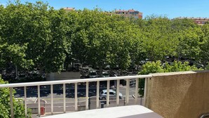 Un balcon avec une table et une chaise blanches, donnant sur un parking et des arbres.