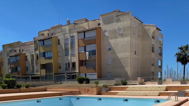 Une piscine dotée d’une terrasse carrelée, entourée d’un immeuble à plusieurs étages avec des balcons.