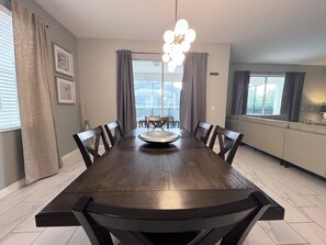 Un coin repas avec une grande table en bois, des chaises foncées, une assiette décorative et un lustre.