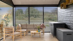 Un'area relax esterna moderna con un patio in legno, un divano, sedie, un tavolino e un angolo barbecue.
