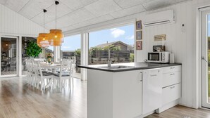 Una cucina moderna con mobili bianchi, un'isola centrale e un'area pranzo con sedie bianche.