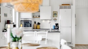 Una cucina moderna con mobili bianchi, forno integrato e frigorifero. È presente un'area pranzo con tavolo e sedie bianche.