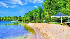 A sandy beach with clear water, a gazebo, and dense trees in the background.