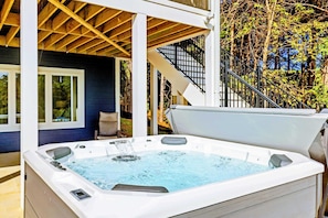A hot tub with a wooden deck and stairs leading to a covered area.
