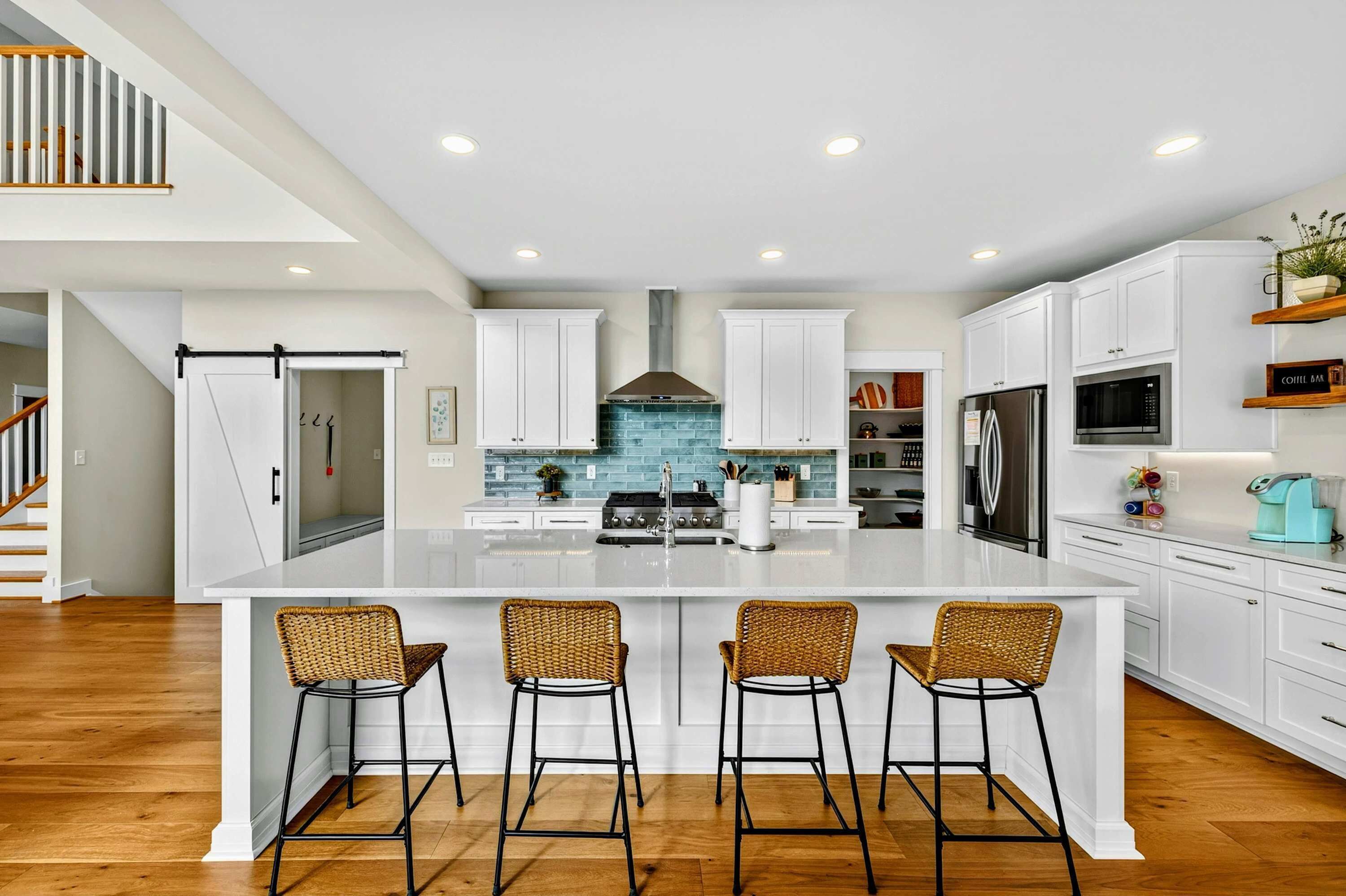 A modern kitchen with white cabinetry, a large island with bar stools, a stainless steel refrigerator, and a blue-tiled backsplash.