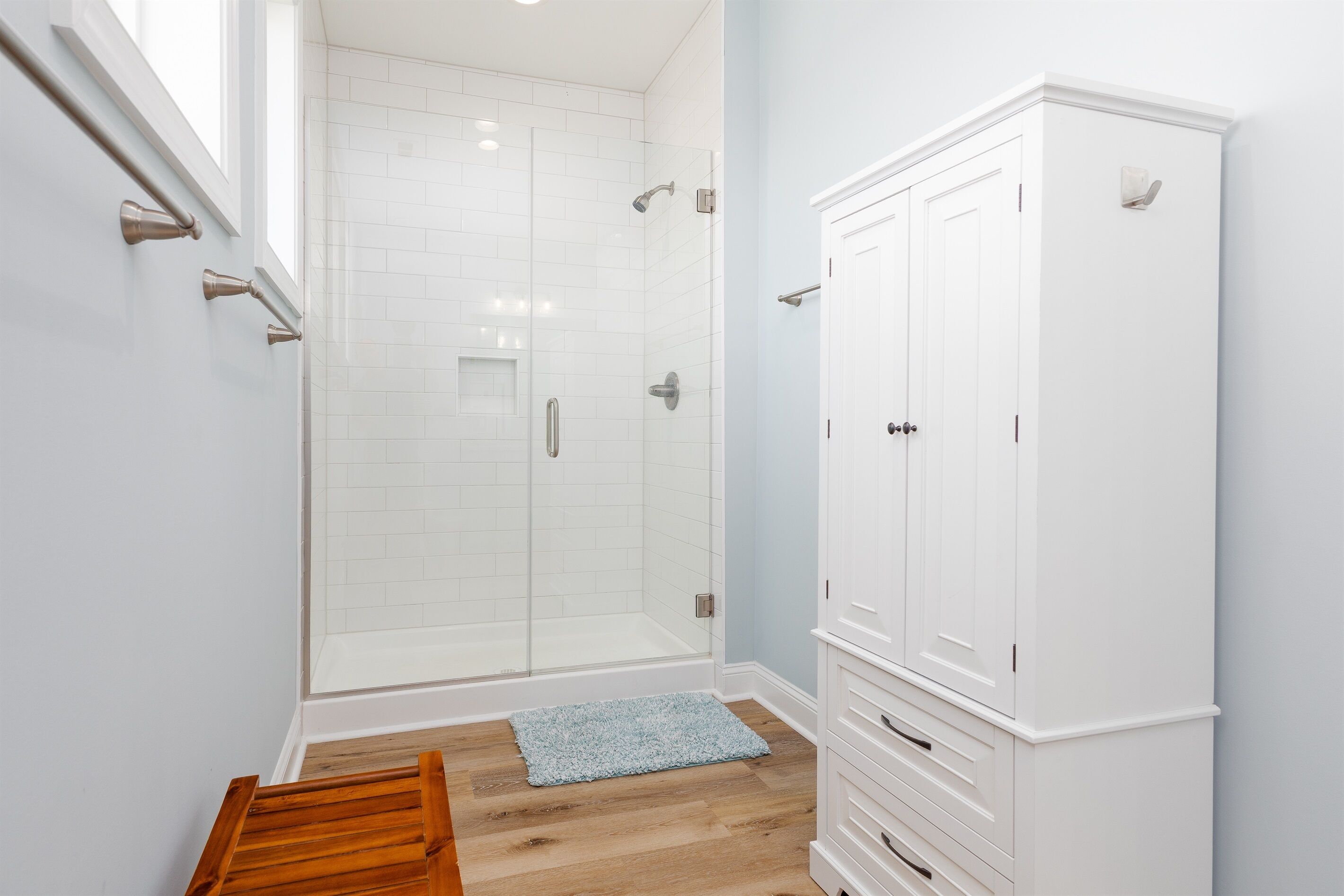 A bathroom with a glass shower enclosure, white cabinetry, and a wooden bench.