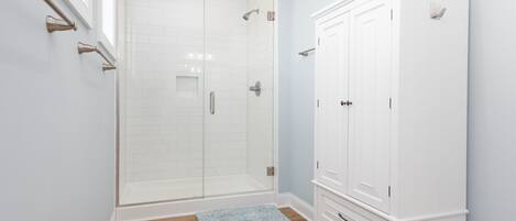 A bathroom with a glass shower enclosure, white cabinetry, and a wooden bench.
