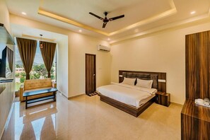 A modern bedroom with a large bed, a bench, a ceiling fan, and a view of greenery outside.