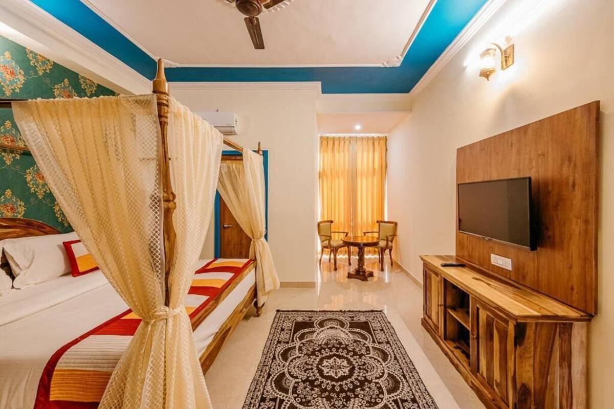 A hotel room with a bed, a TV, a ceiling fan, and a dining area with chairs and a table.