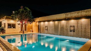 A swimming pool with a clear blue water surface, surrounded by a low brick wall and a wooden deck. - Aditya Palace (Pushkar)