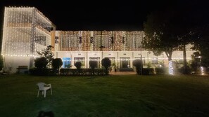 A building with a covered outdoor area, string lights, and a lawn.