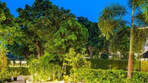 An outdoor dining area with multiple tables and chairs, surrounded by lush greenery and trees. - Aditya Palace (Pushkar)