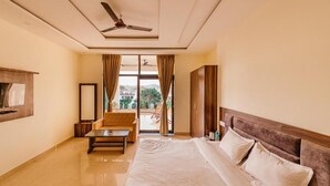 A hotel room with a bed, a sofa, a coffee table, a TV, and a view of the outdoors. - Aditya Palace (Pushkar)