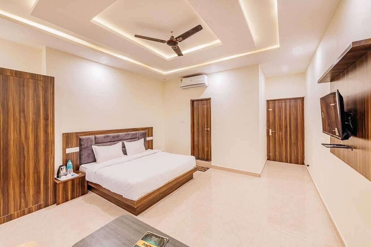 A modern hotel room with a wooden bed, a ceiling fan, an air conditioning unit, and a television mounted on the wall.