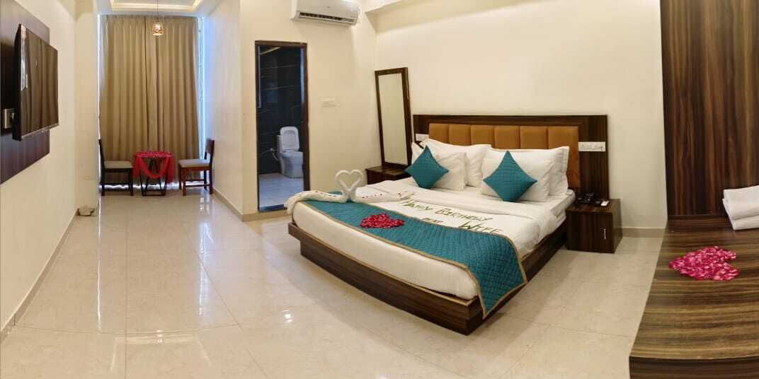 A hotel room with a large bed, a bedside table, a TV, and a bathroom visible through an open door.